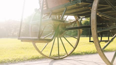 the wheel of a historic carriage rotates on a sandy path with the sunrise in the background