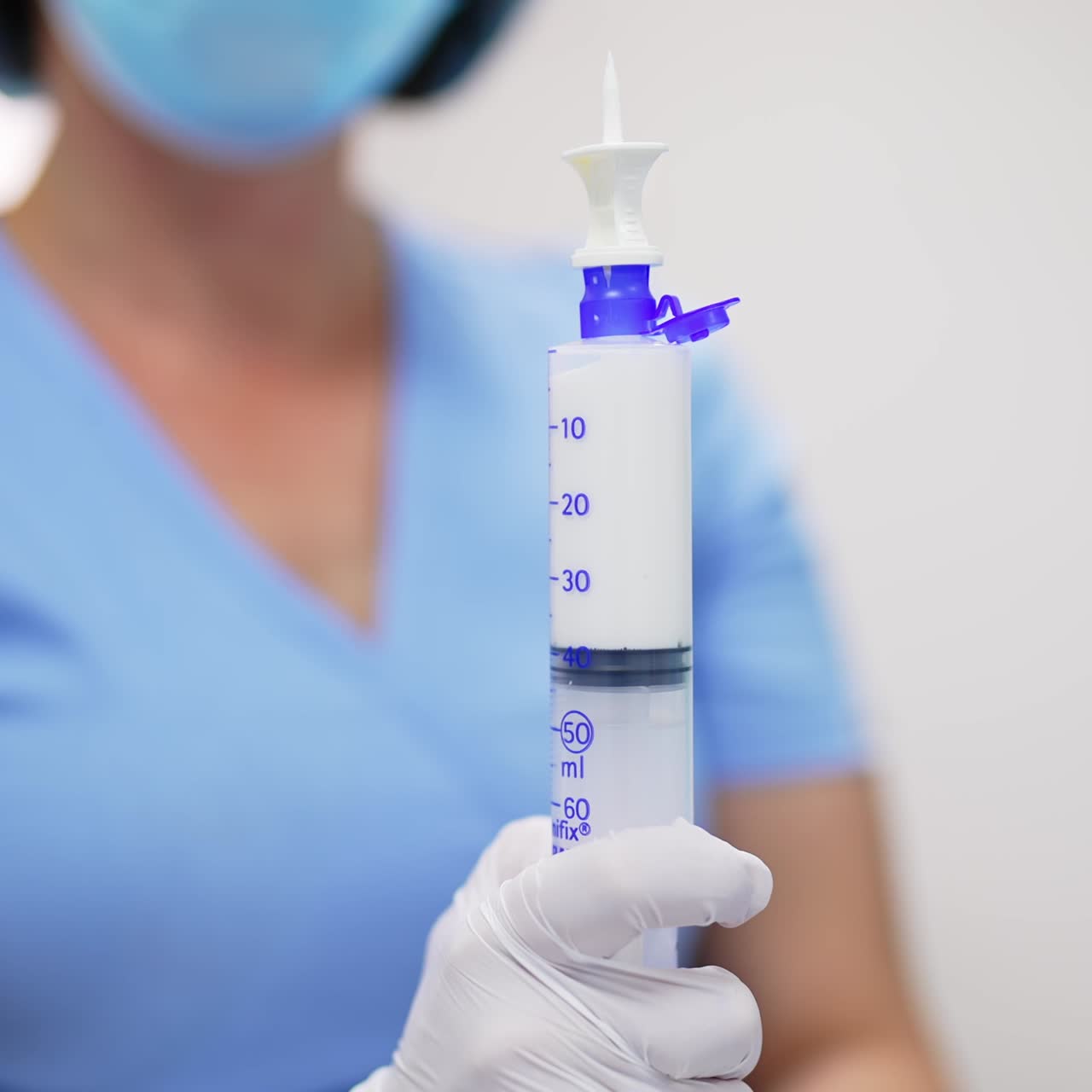 Female nurse holding a syringe filled with white medicine. Close up. Blurred backdrop