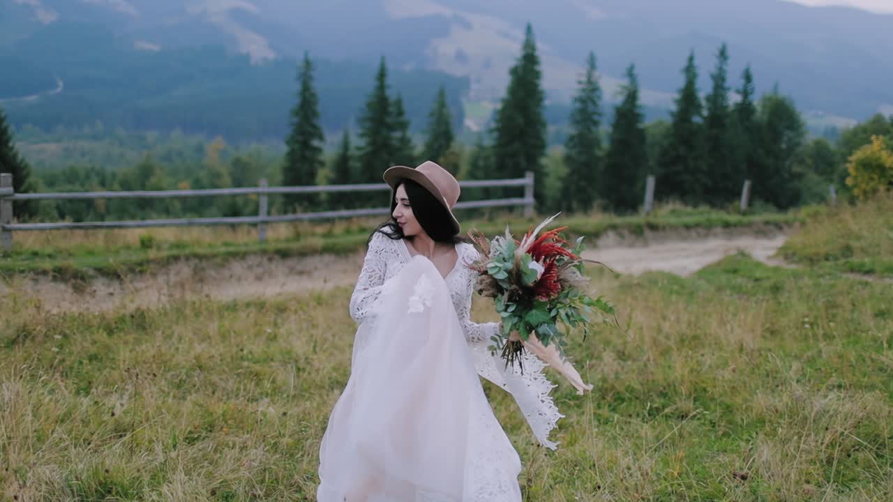 Beautiful bride against mountains. Beautiful woman in wedding dress walks along green plants in mountains