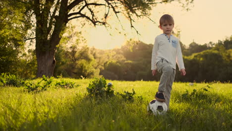 in slow motion the boy plays funny with a soccer ball in a meadow at sunset