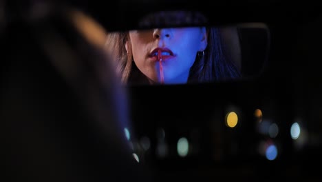 attractive woman apply red lipstick on her lips using car rear view mirror at night