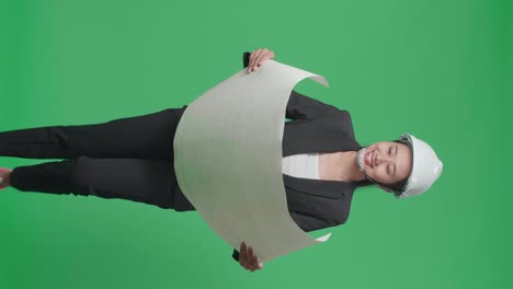 smiling asian female engineer with safety helmet looking at blueprint while walking in the green screen studio