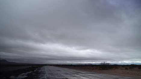 Cloudscape-over-a-wet-Mojave-Desert-road-through-the-wilderness-after-a-rare-winter-thundershower---time-lapse