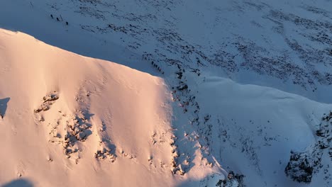 Drone-shot-of-Musala-peak-during-sunrise,-Bulgaria,-Rila-mountain,-highest-summit-on-the-Balkans,-people-walking-down-the-sunny-slope,-golden-hour,-blue-hour,-dawn