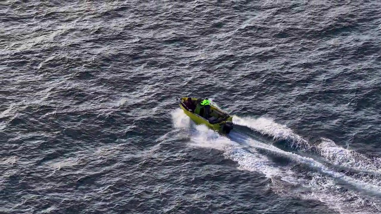 Rekaman udara sudut tinggi sebuah perahu motor kuning menciptakan jejak putih di air laut biru