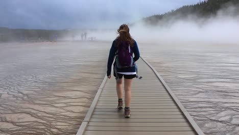 a girl walking on a boardwalk in yellowstone national park
