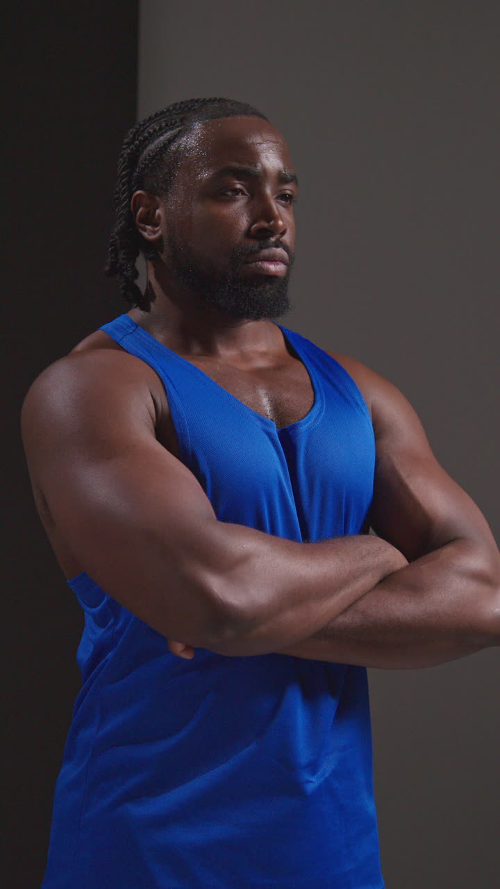 fotografía de estudio de video vertical de un atleta masculino con chaleco sudando después de un entrenamiento deportivo o haciendo ejercicio en el gimnasio doblando los brazos