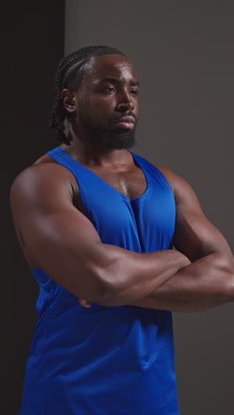 vertical video studio shot of male athlete wearing vest sweating after sport training or exercising in gym folding arms