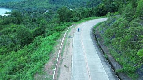 aerial drone footage following a moped driving on a country road in between green mountains in rural philippines