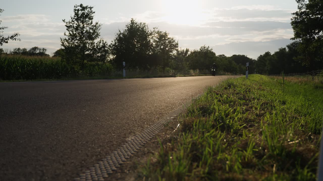 силуэт мужчины на современном спортивном мотоцикле проезжает по асфальтированной дороге в сельской местности на фоне яркого солнца
