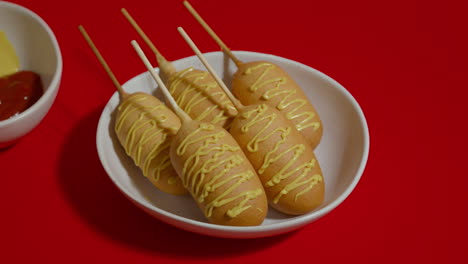 moving shot of red background with white plate and five corn dogs with sauce.