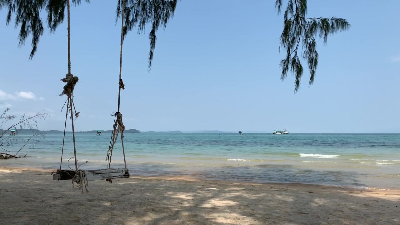 Balanços de corda pendurados em árvores acima de uma costa arenosa em Phu Quoc, enquanto ondas calmas se movem pela água