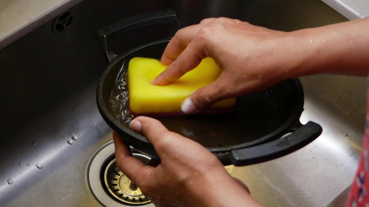Persona lavando una sartén de hierro fundido en un fregadero de cocina