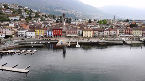 aerial flyover along the shore of lago maggiore and promenade of ascona in ticino, switzerland with a turn over the city rooftops revealing the lake and mountains behind the church tower