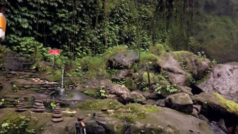 panning view of ubud water fall and lush green jungle wall with religious shrine honouring balinese gods