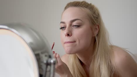 blond female applying lip liner near mirror