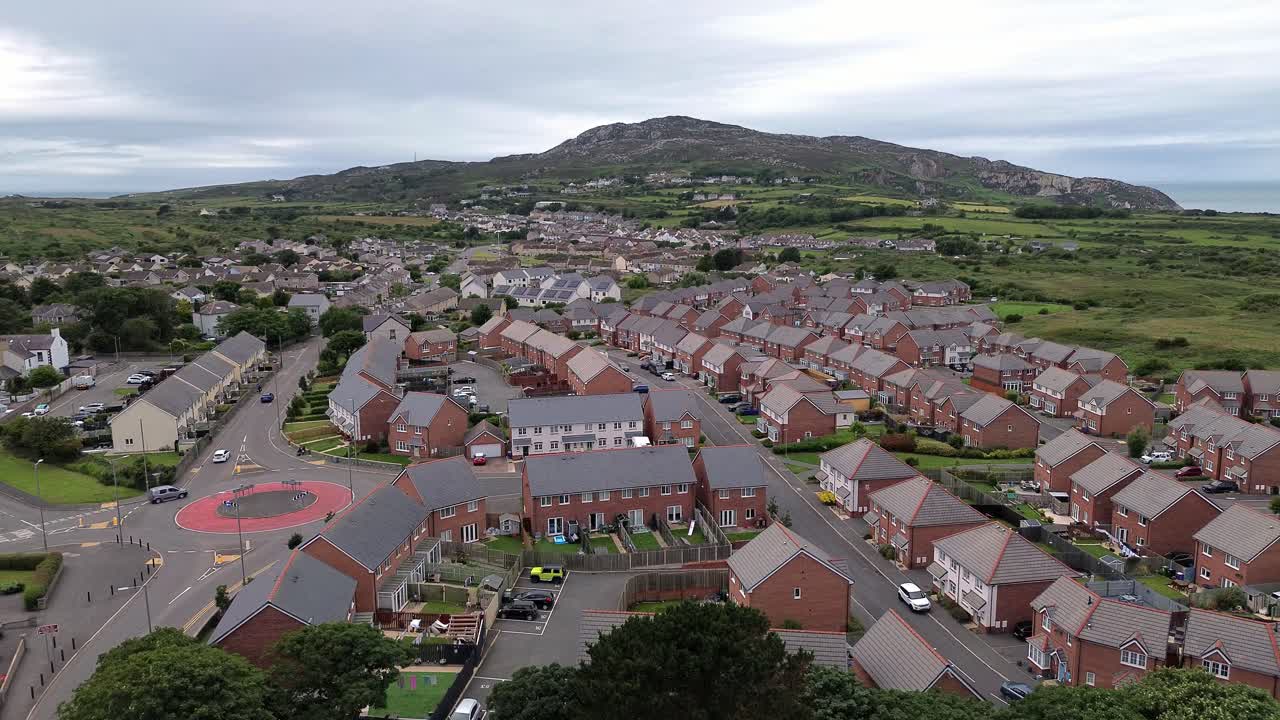 Aerial rising view over modern red brick housing neighbourhood under Holyhead mountain in Wales