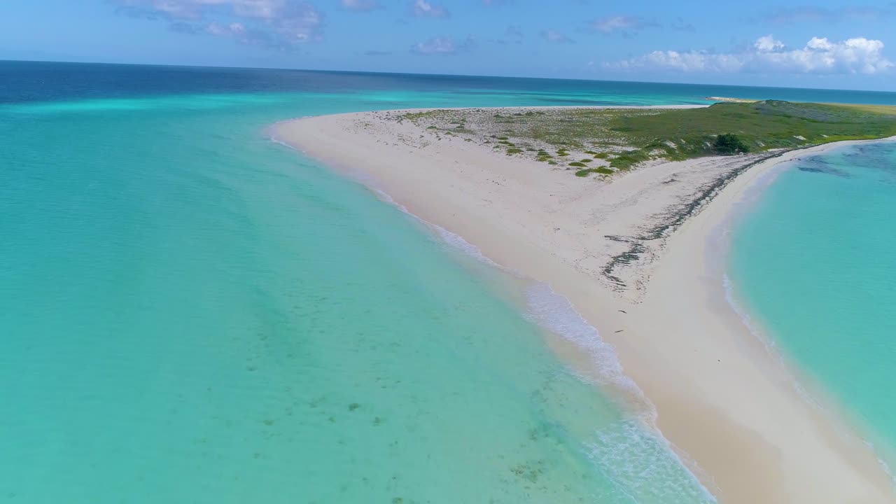 drone filmó un banco de arena tropical con 2 personas caminando en una playa de arena blanca, salpicaduras de agua turquesa en la arena, cayo de agua los roques