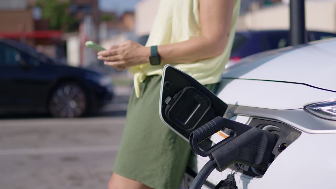 женщина заряжает электрический автомобиль смартфоном