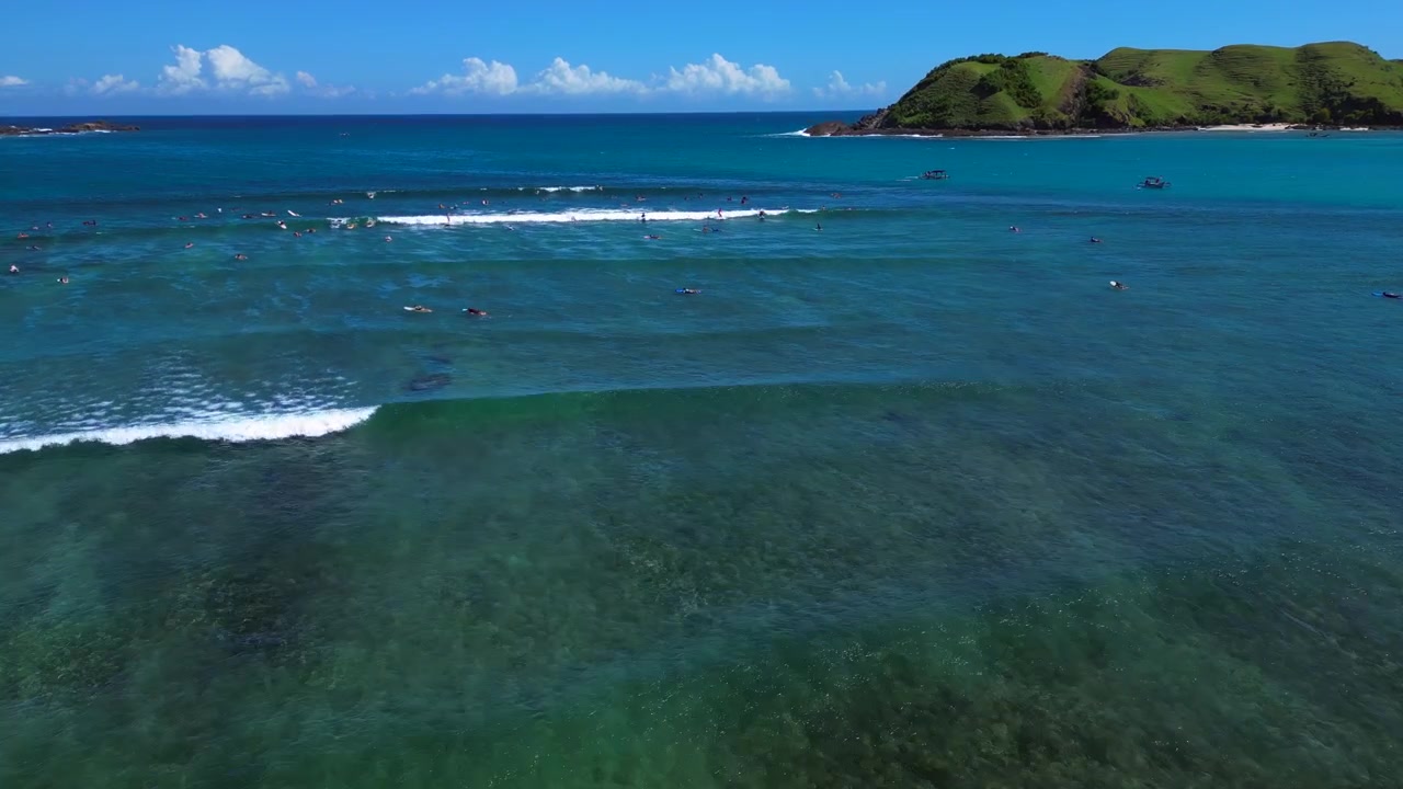 Surfer som rir på en bølge med mange andre surfere som venter i det fjerne. Havet er klart blått under en solrik himmel. Nydelig luftfoto, oversikt, panorama, drone.