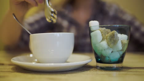 mujer poniendo azúcar en la taza de té usando pinzas