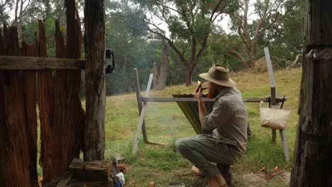un bosquero enciende su pipa usando una fogata mientras está en un refugio de corteza en el bosque australiano