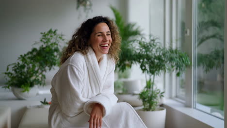 woman in bathrobe laughing in a bright, plant-filled room