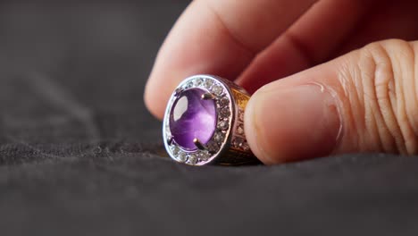 primer plano de una mano sosteniendo un anillo de oro con una gran piedra preciosa de ametista