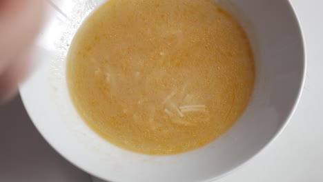 a hand stirs cocido soup in a bowl, showcasing the golden broth and ingredients