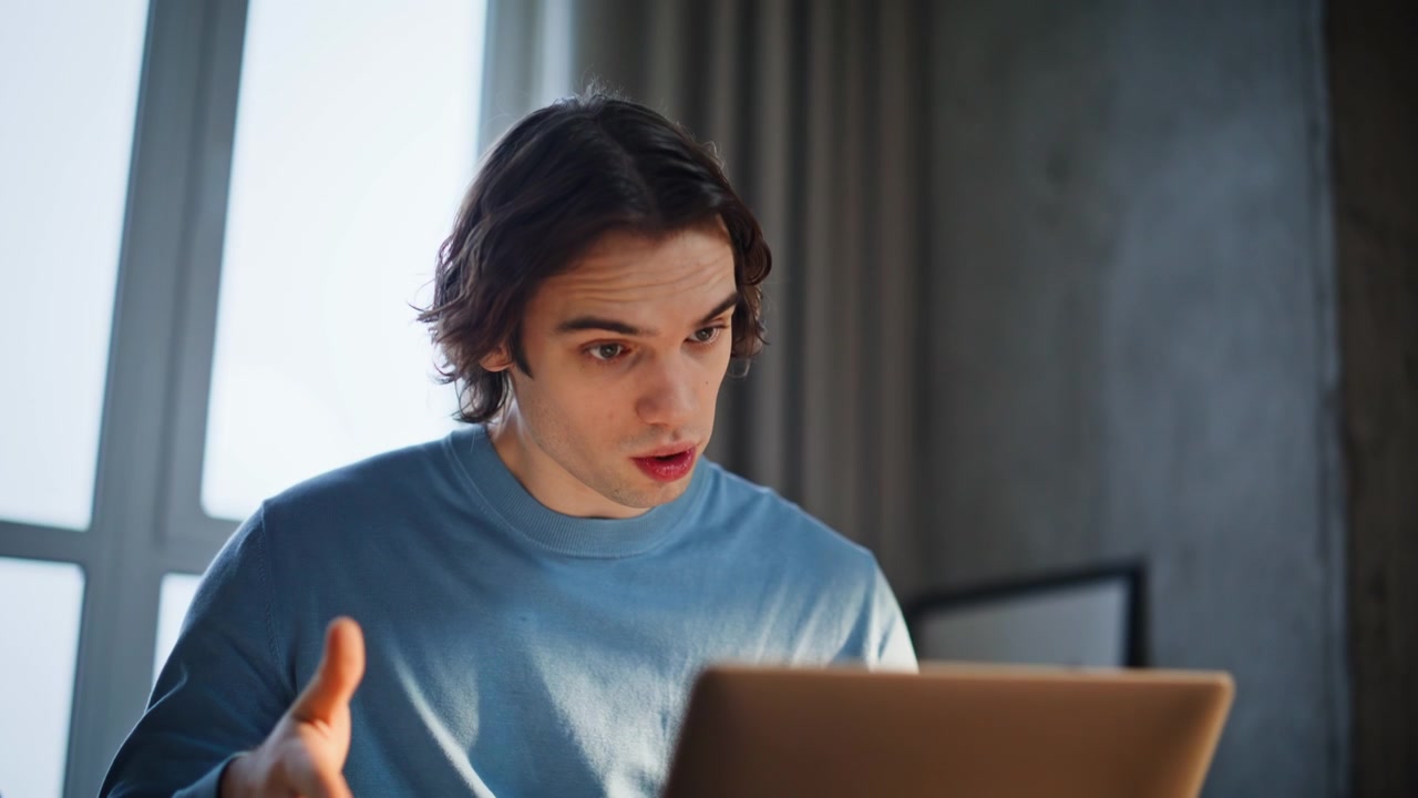 Primo piano di un manager online che saluta, lavora al laptop seduto nella camera da letto di un appartamento.