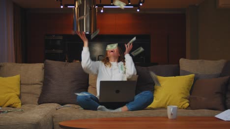 mujer joven afortunada con computadora portátil ganar dinero lluvia, sentado en el sofá en casa. éxito financiero, victoria en el casino en línea, premio mayor