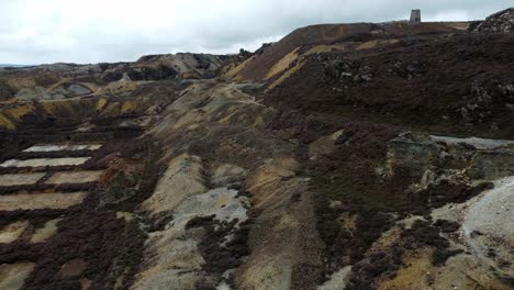 Parys-mountain-abandoned-historic-copper-mine-red-stone-mining-industry-landscape-aerial-rising-right-orbit-view