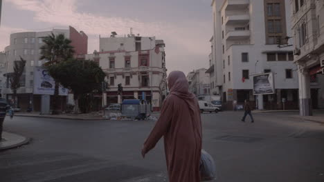 una mujer árabe musulmana marroquí con hiyab y vestido tradicional cruza la calle en el bonito barrio de casablanca