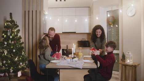 father and mother give christmas gifts to their children during christmas dinner and sit at the table