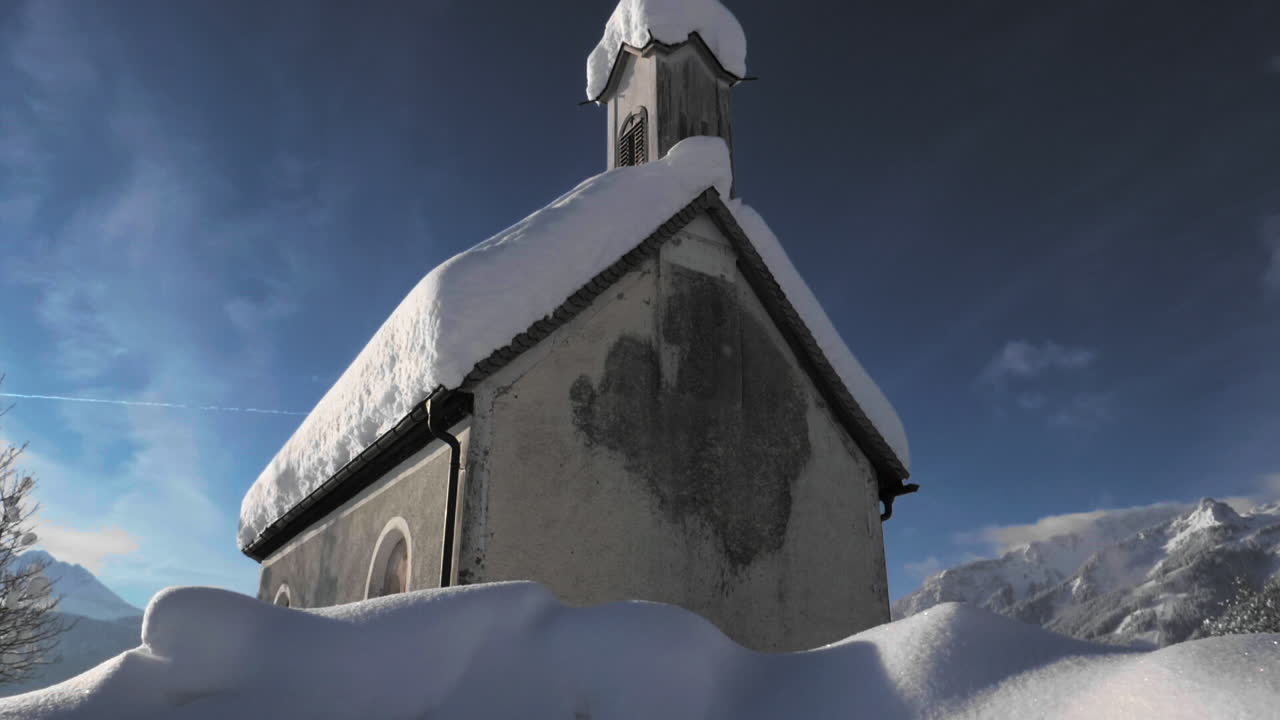 Gimbal shot showing a snowy landscape in in the sunshine of the Tyrol, Austria and revealing a snow covered tiny chapel in Lechaschau