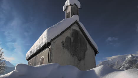gimbal shot showing a snowy landscape in in the sunshine of the tyrol, austria and revealing a snow covered tiny chapel in lechaschau