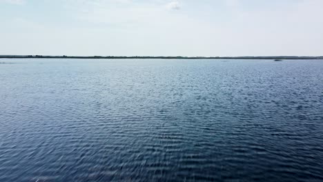 aerial flyover above a tranquil lake pape surface in calm summer day, wide angle drone shot moving backwards, camera tilt down