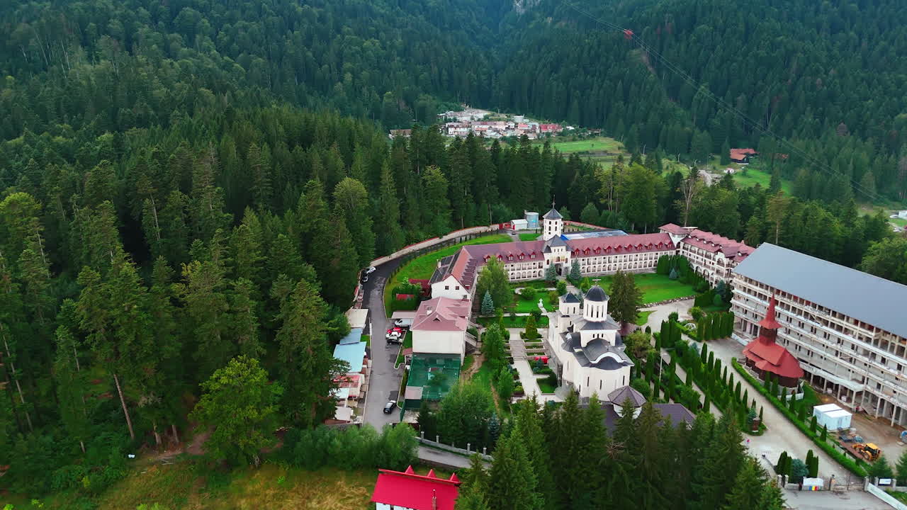 Beautiful buildings and churches on the mountain surrounded by the pine tree woods. Drone flight above Busteni, Romania