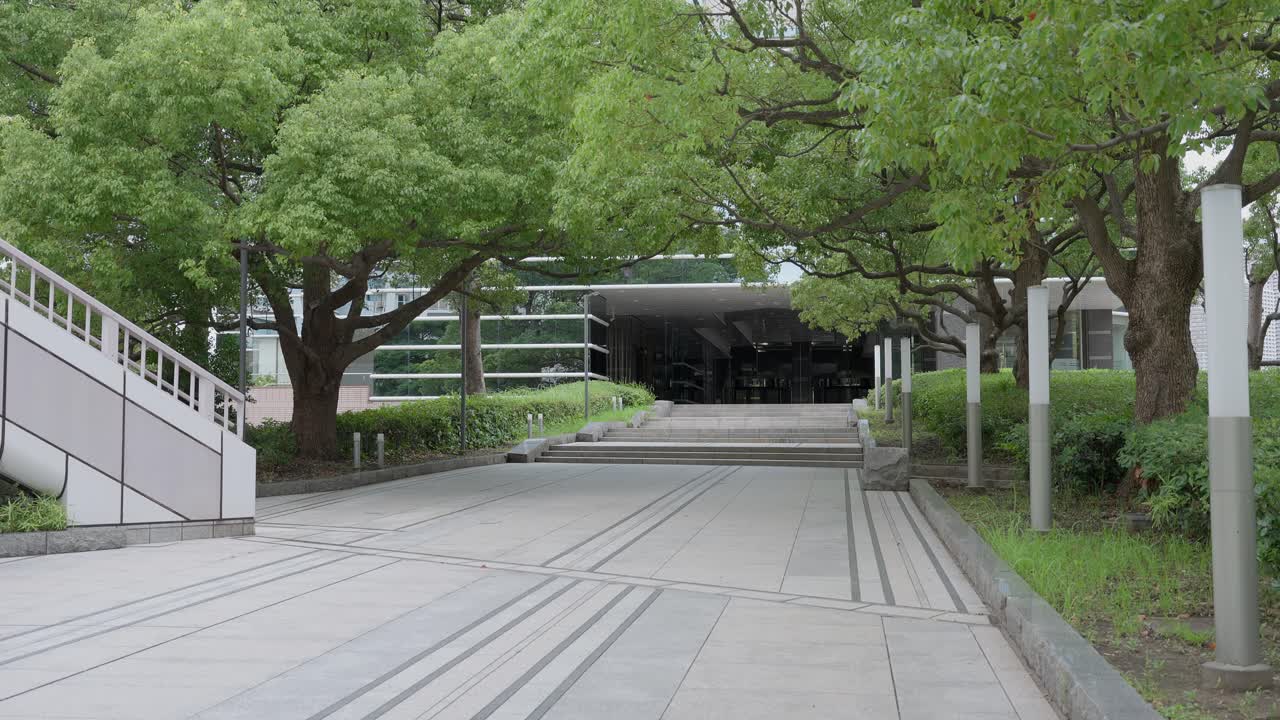 A peaceful shot of a paved walkway leading toward a modern building, surrounded by green trees and foliage