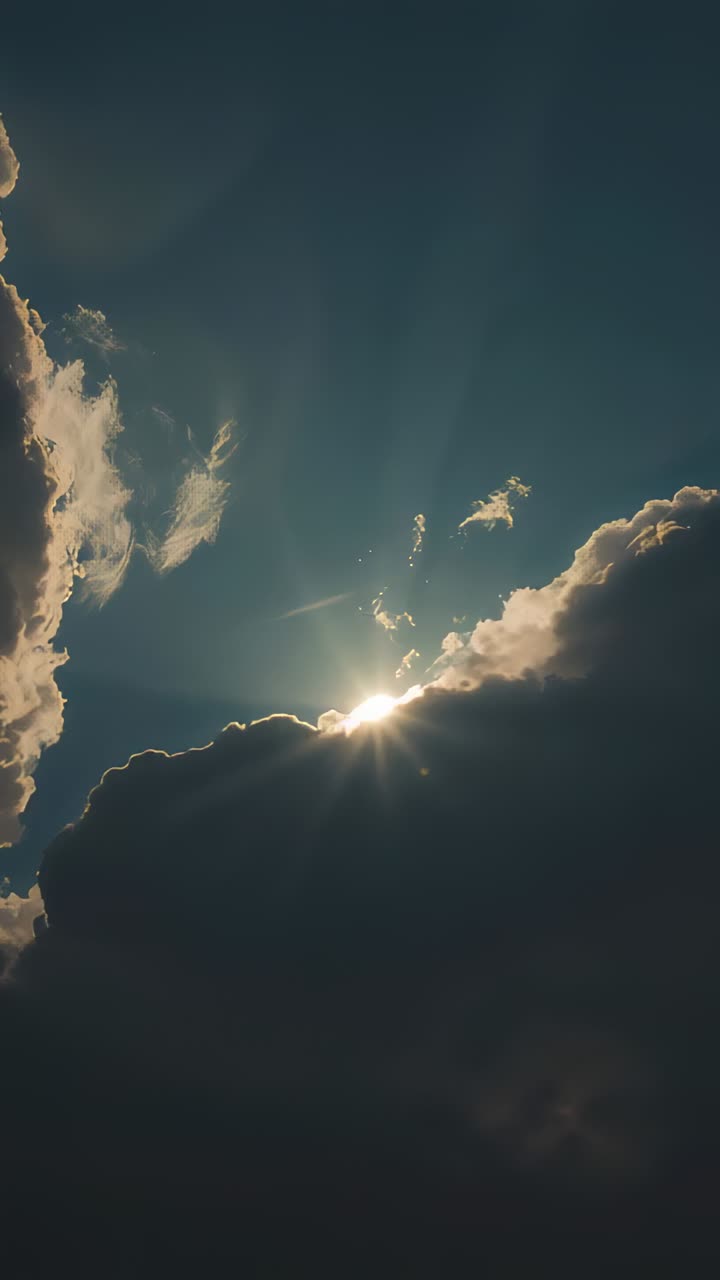 Vertical video: Peeking sun casting rim light over dark cloud bank in deep blue sky forming rays