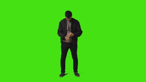 Smiling-Young-Man-Answering-Call-On-Mobile-Phone-Standing-Against-Green-Screen-Studio-Background-1