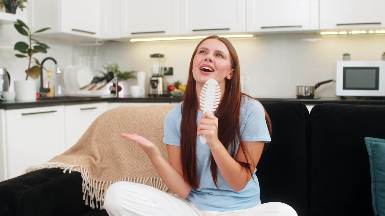 Giovane donna canta in un pettine per capelli come fosse un microfono, balla al ritmo della sua canzone preferita, sognando di essere una star, in un'atmosfera giocosa