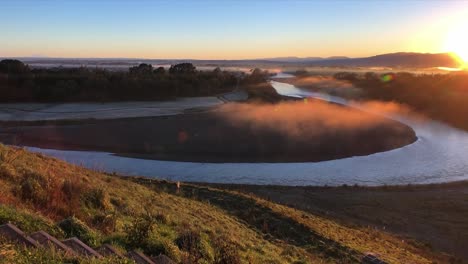 zoom lento de una vista sobre un río brumoso de nueva zelanda con el brillo dorado del sol naciente