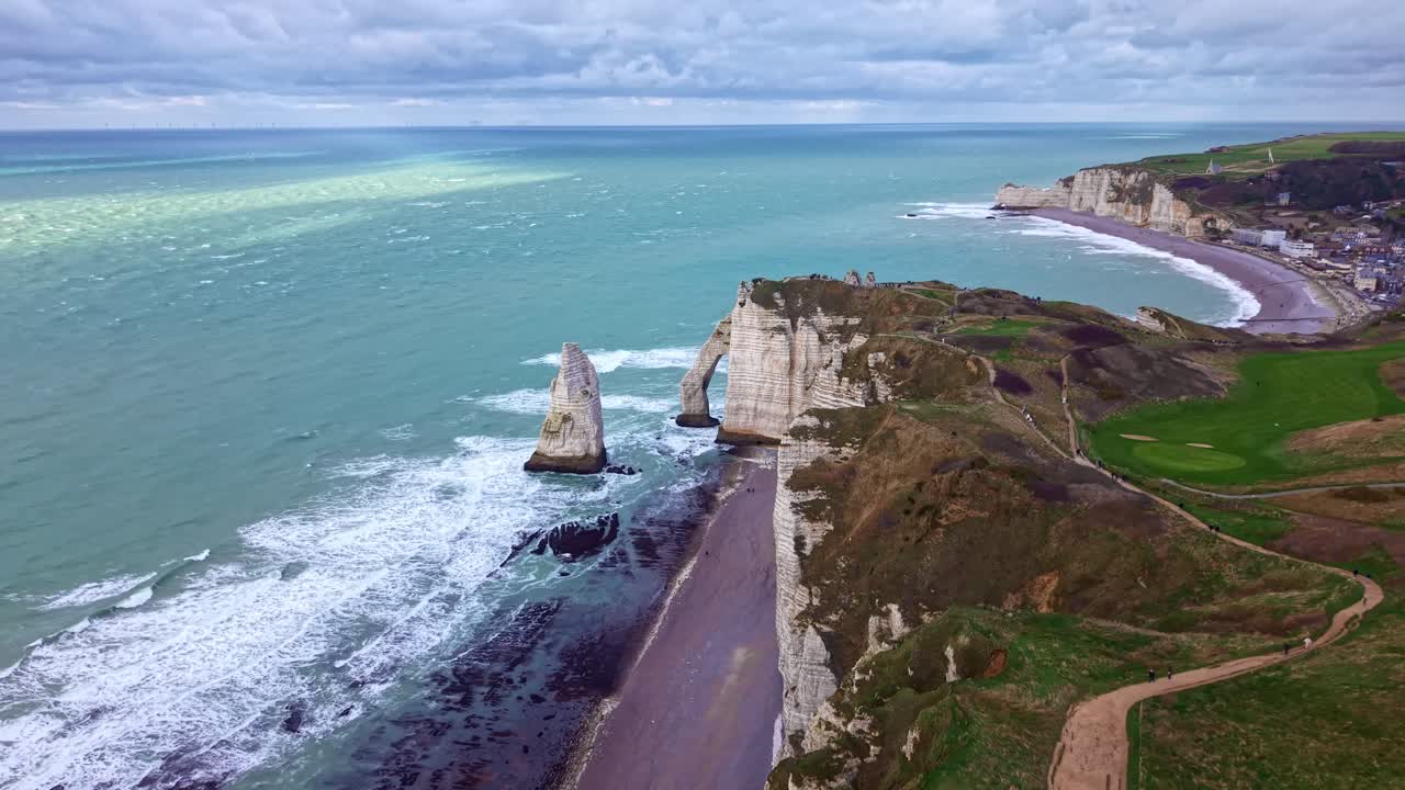 Majestic aerial drone view of the iconic Falaise d'Aval and Aiguille rock formations in Etretat. The waves of the English Channel crash against the dramatic cliffs, France
