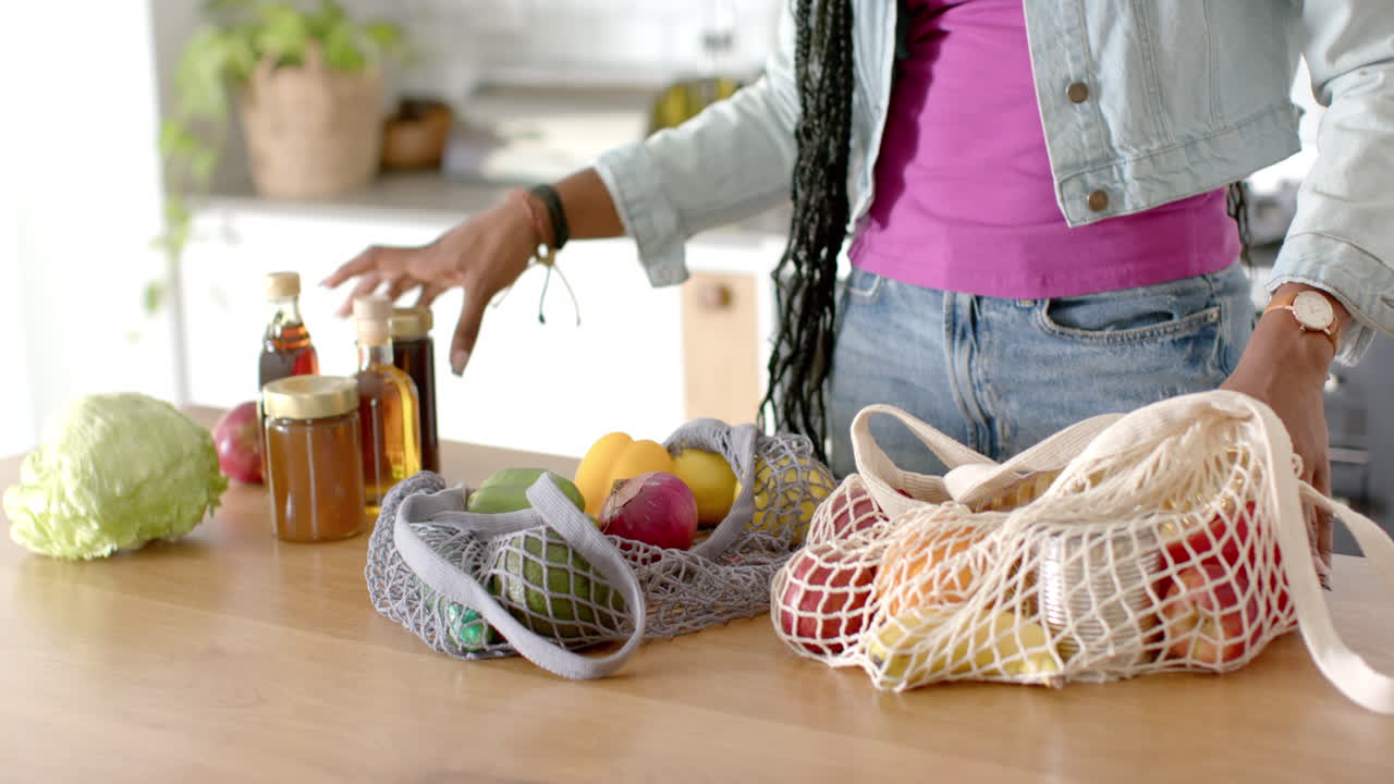 African American young woman unpacking groceries in kitchen, at home, copy space