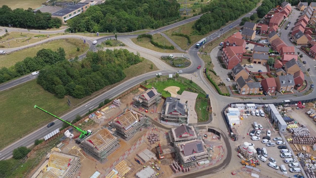 Nye boliger under utvikling med kraner og kjøretøy parkert i nærheten på en lys solrik ettermiddag i England, mens arbeidere fortsetter å bygge hus i et forstadsboligområde.
