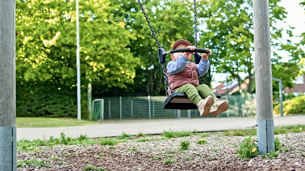 Un bambino felice d'estate si dondola sull'altalena di sera in un parco giochi pubblico. Concetto di infanzia spensierata.