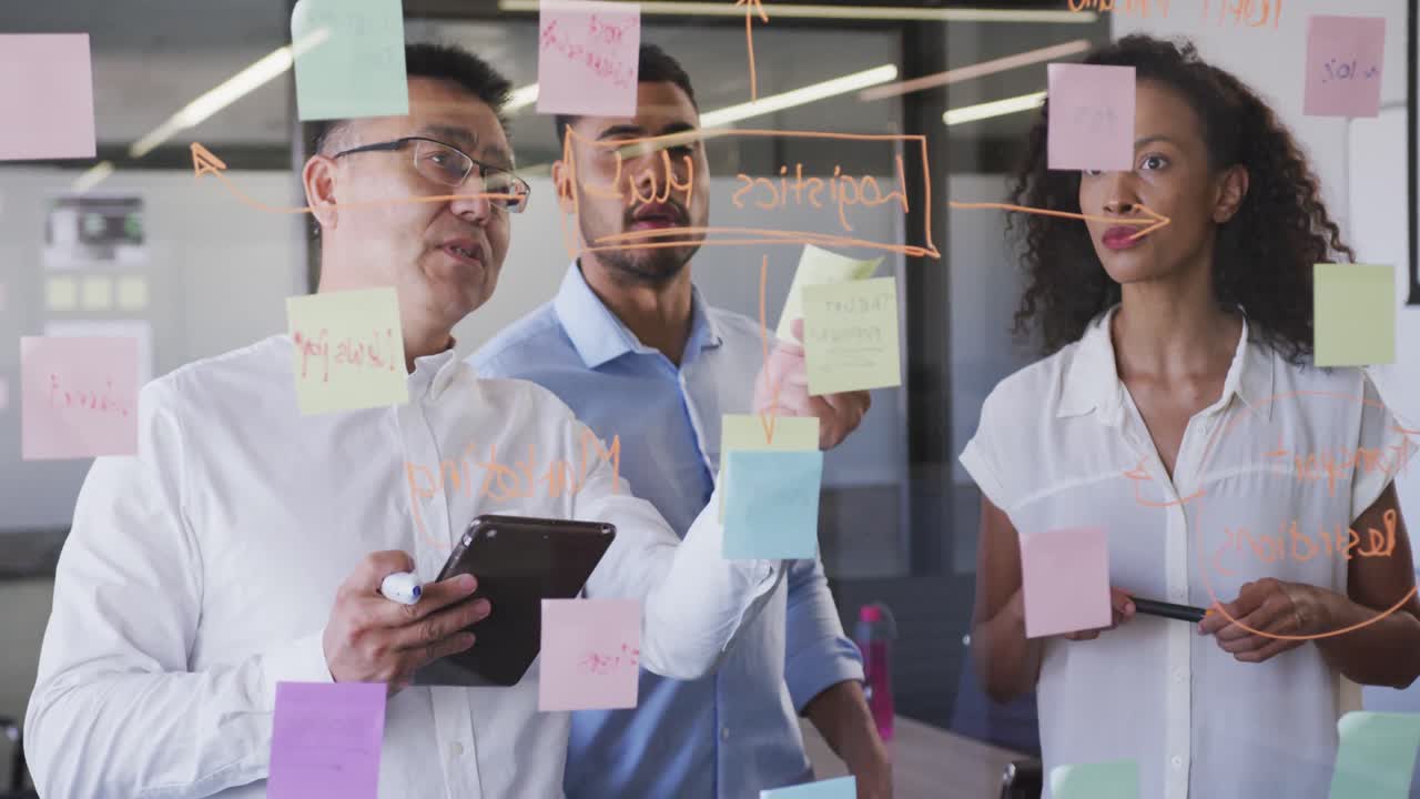 Senior businessman discussing with young business people over memo notes on glassboard in office
