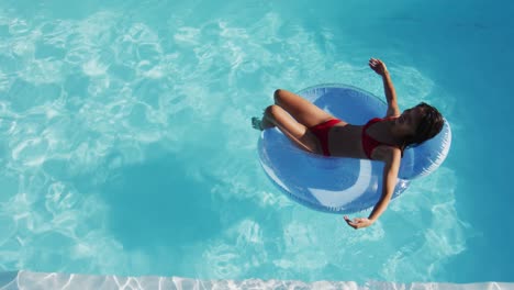 Mixed-race-woman-having-fun-sunbathing-on-inflatable-in-swimming-pool