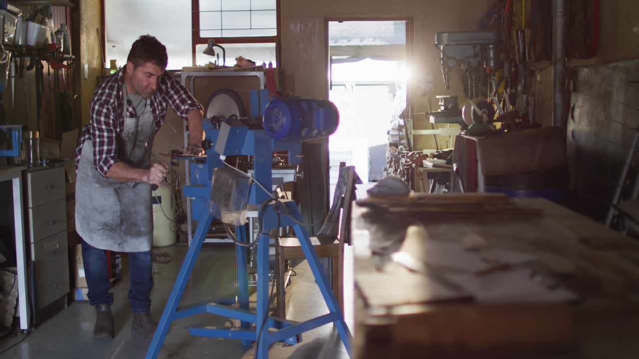 Focused caucasian male knife maker in workshop using saw